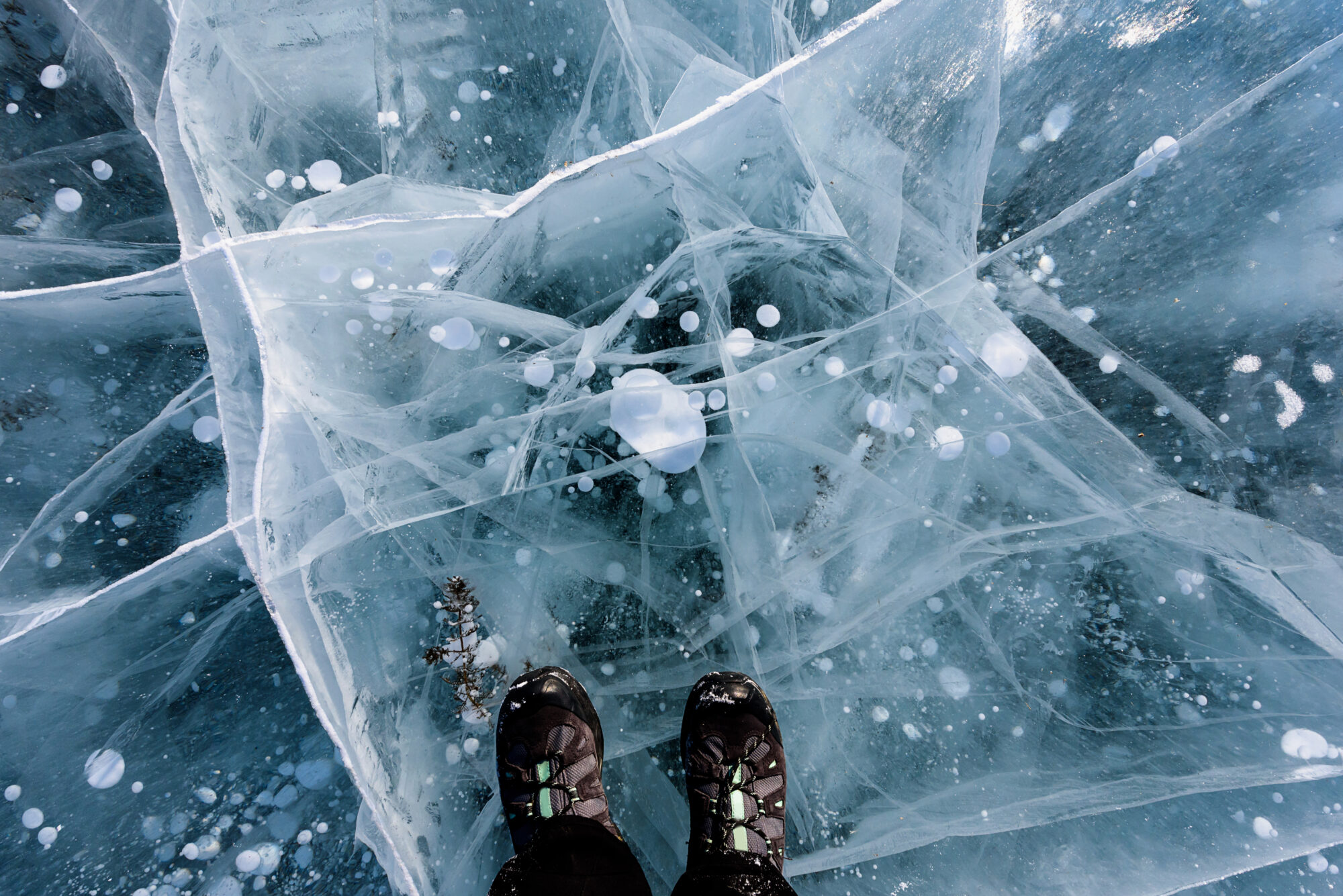 Beautiful blue ice of Lake Baikal with abstract cracks with black shoes. Top view